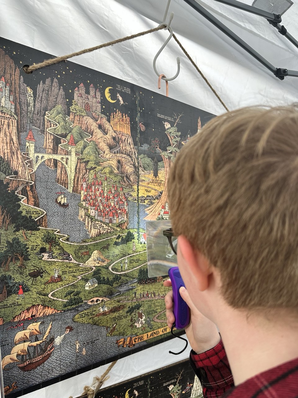 Flat lay of The Land of Make Believe wooden puzzle completed, showing vibrant fairytale map artwork by Jaro Hess. A kid watching Jaro Hess' artwork with a magnifier