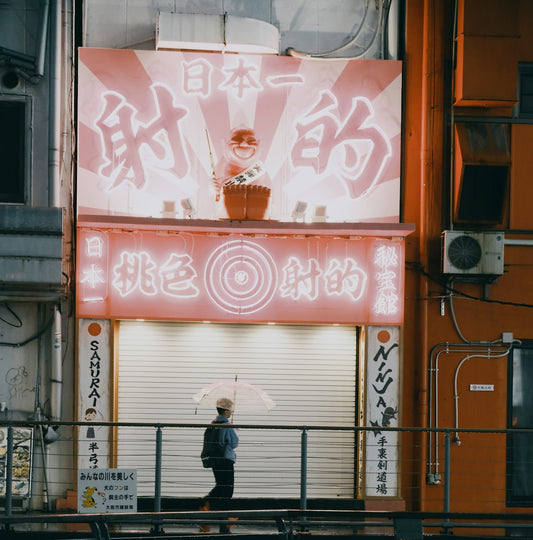 Person with umbrella walks past glowing japanese signs
