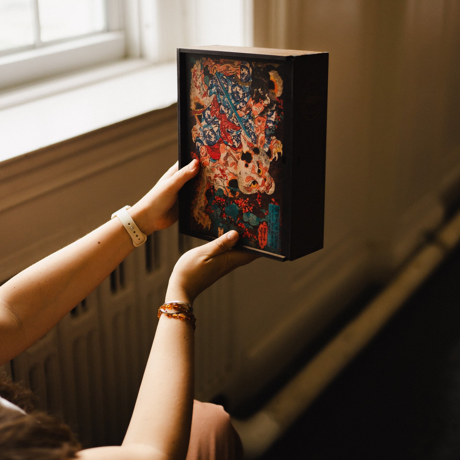 A person is holding a framed artwork with a colorful, abstract design on the back cover.