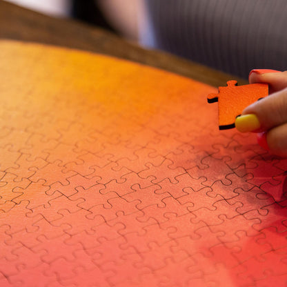 A person's hand holding a puzzle piece is partially visible, with the puzzle pieces arranged in a circular pattern on a surface.