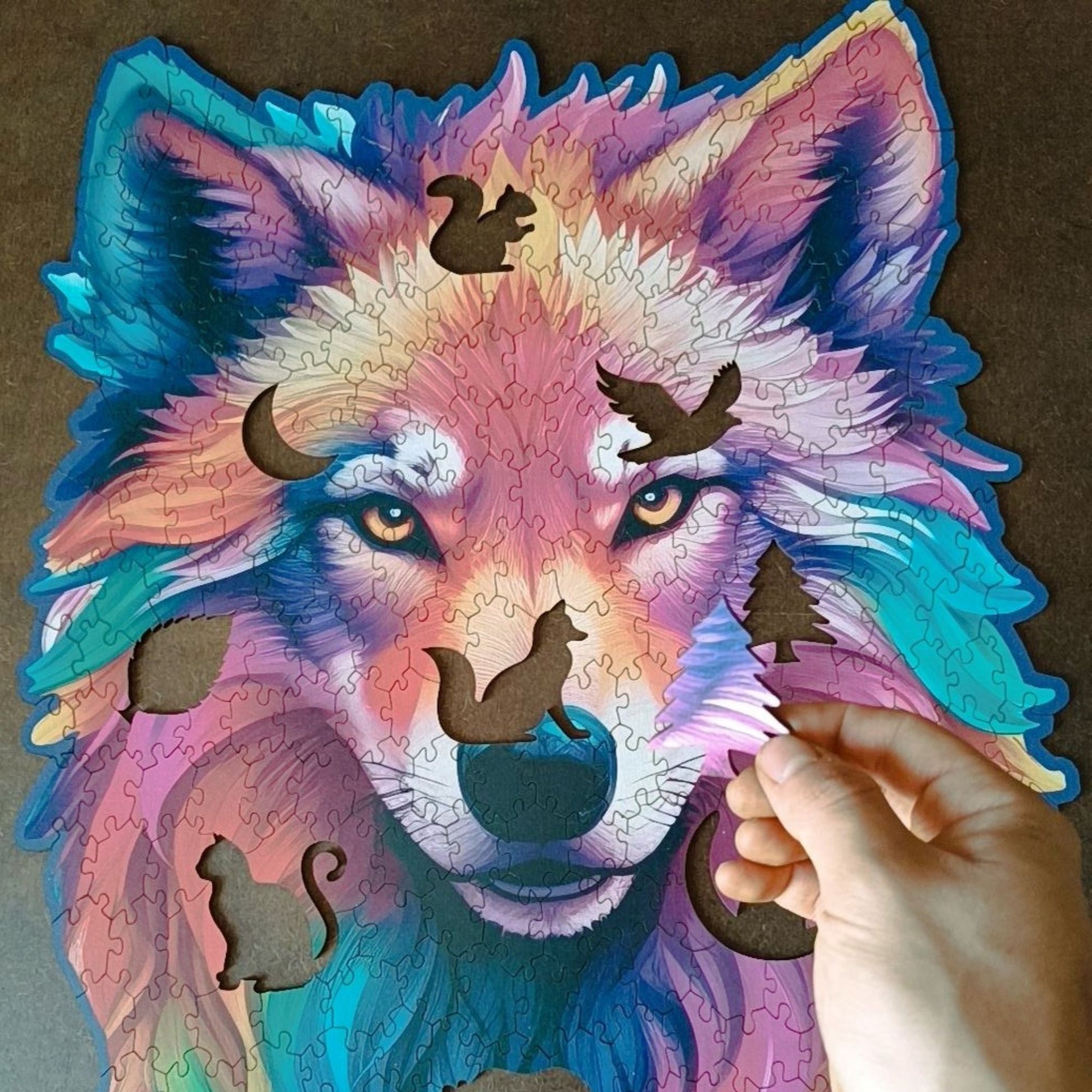 A hand holding a jigsaw piece. A wooden jigsaw puzzle grid of a dark, almost black background that contrasts with the vibrant colors of the wolf, making it the focal point.