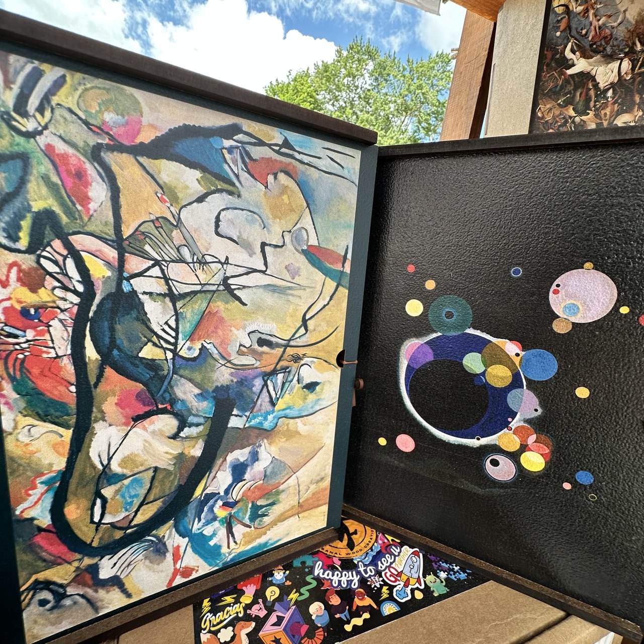 two framed abstract paintings displayed side by side. The left frame is a vibrant, colorful abstract painting with bold brushstrokes and a mix of geometric and organic shapes. The right frame is a black and white abstract painting with a more minimalist and monochromatic style.