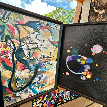 two framed abstract paintings displayed side by side. The left frame is a vibrant, colorful abstract painting with bold brushstrokes and a mix of geometric and organic shapes. The right frame is a black and white abstract painting with a more minimalist and monochromatic style.
