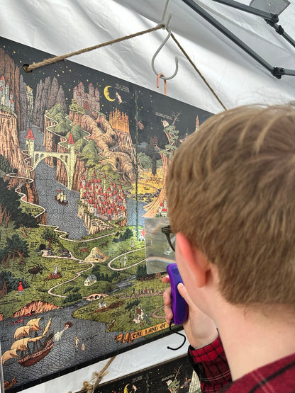 Flat lay of The Land of Make Believe wooden puzzle completed, showing vibrant fairytale map artwork by Jaro Hess. A kid watching Jaro Hess' artwork with a magnifier