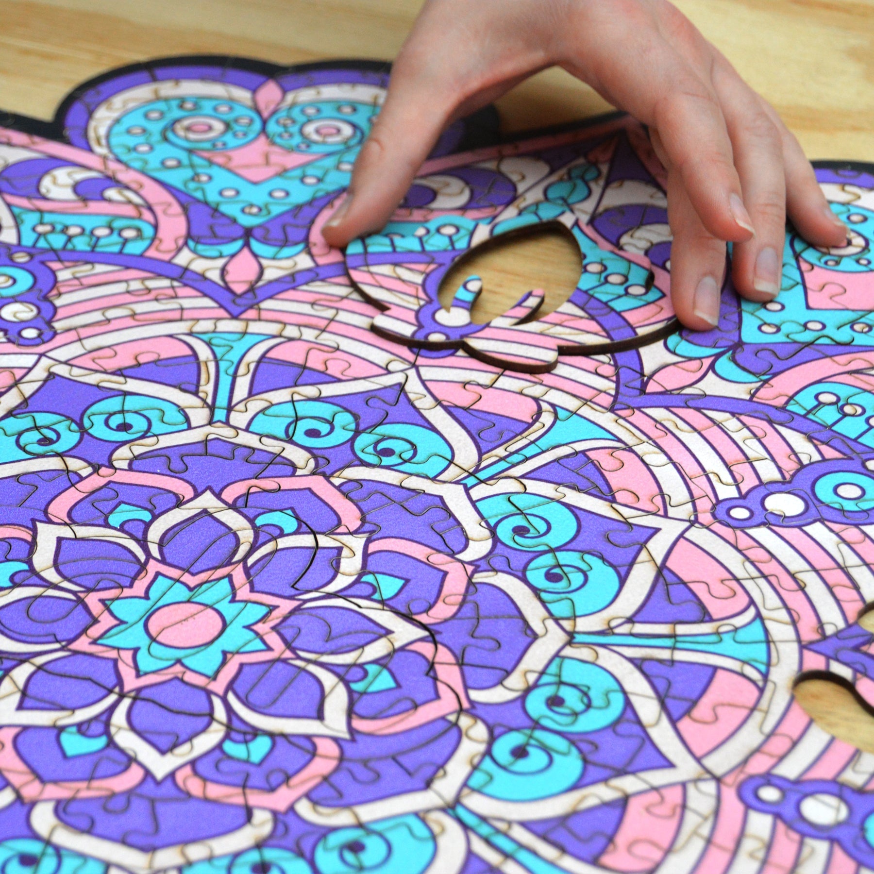 hands holding jigsaw pieces of a colorful mandala wooden jigsaw puzzle with a geometrical design.