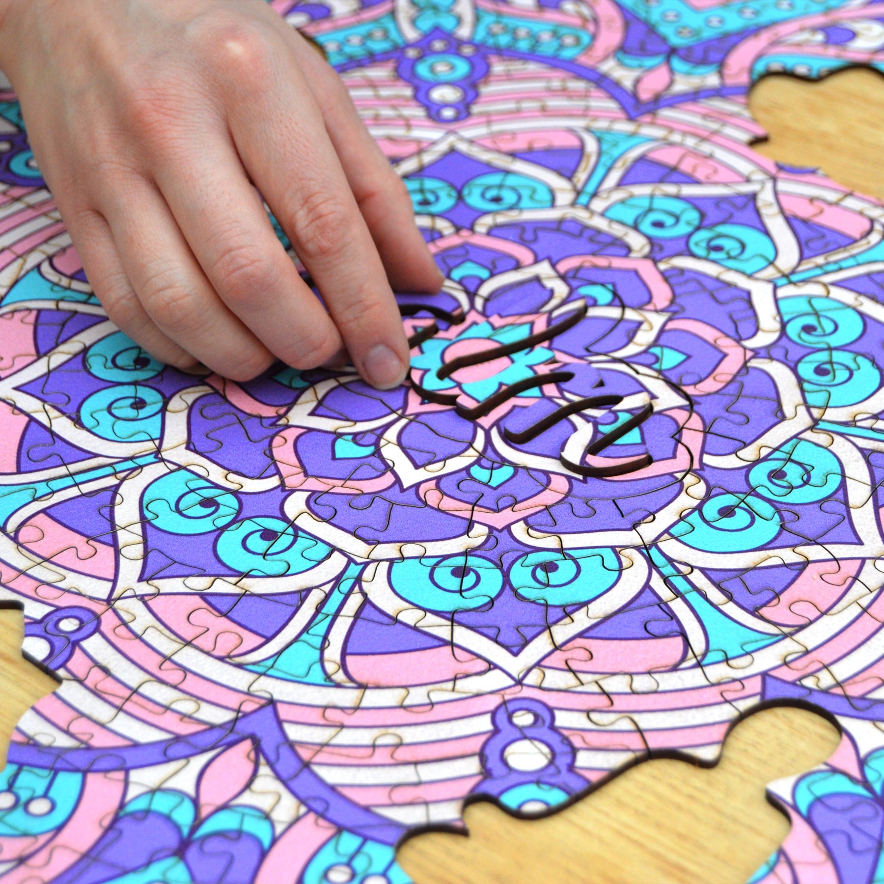hands holding jigsaw pieces of a colorful mandala wooden jigsaw puzzle with a geometrical design.