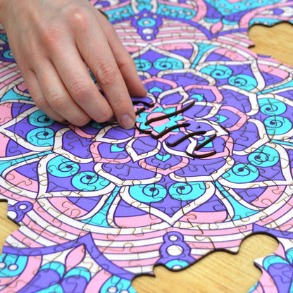 hands holding jigsaw pieces of a colorful mandala wooden jigsaw puzzle with a geometrical design.