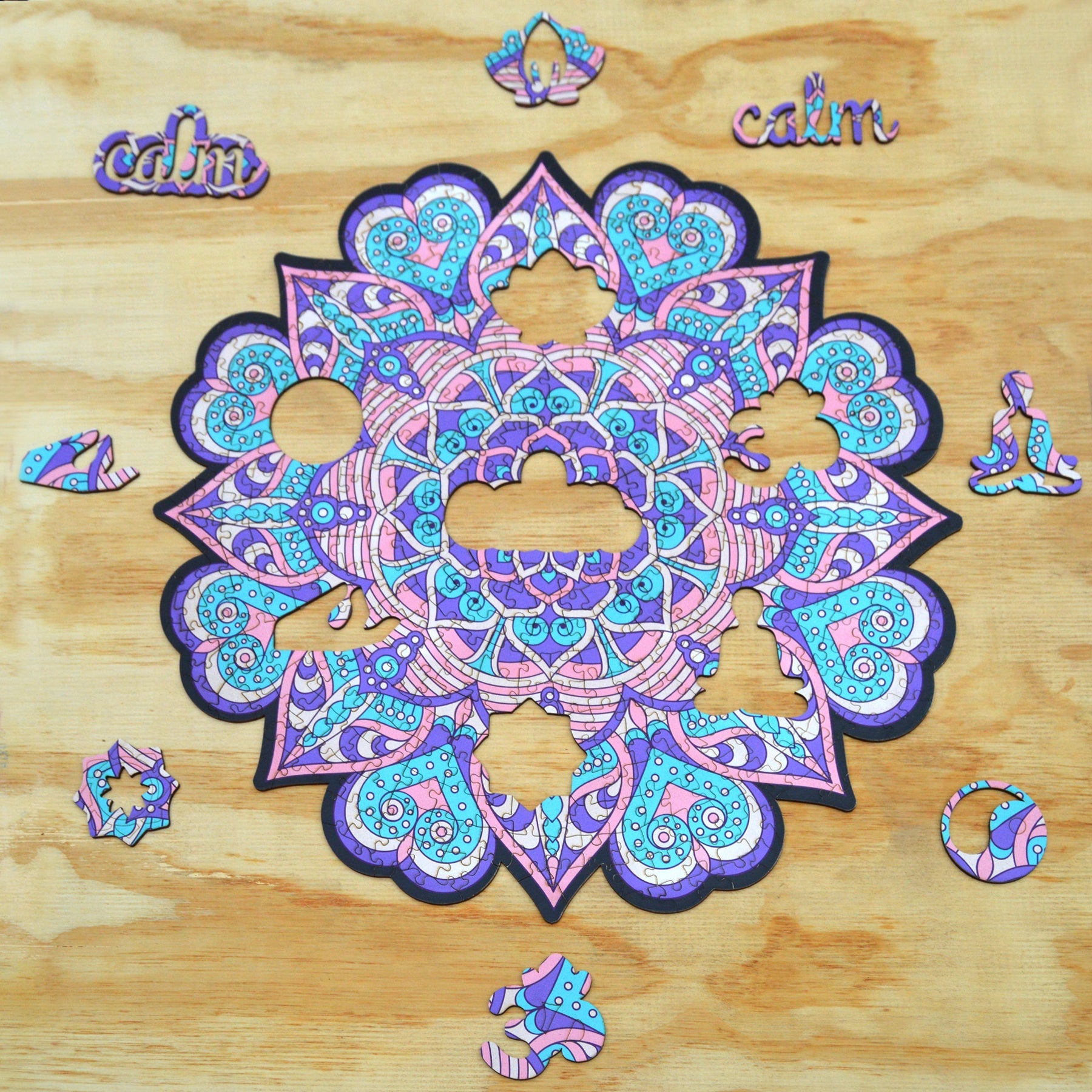 colorful mandala wooden jigsaw puzzle with a geometrical design. pURPLE AND PINK TONES, HAS A CENTRAL FOCAL JIGSAW PIECE THAT READS THE MANTRA calm.