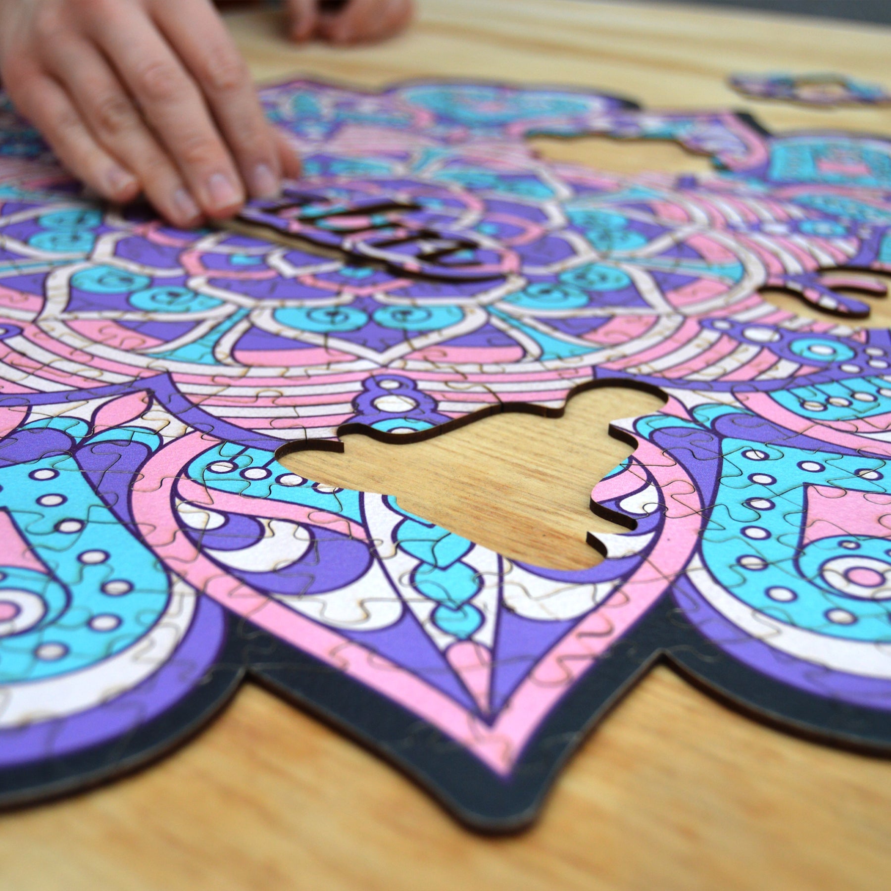 hands holding jigsaw pieces of a colorful mandala wooden jigsaw puzzle with a geometrical design.