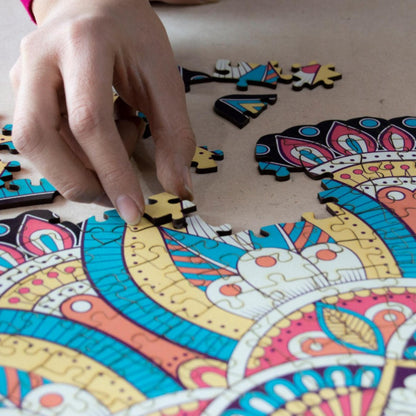 hands holding jigsaw pieces of a colorful mandala wooden jigsaw puzzle with a geometrical design.