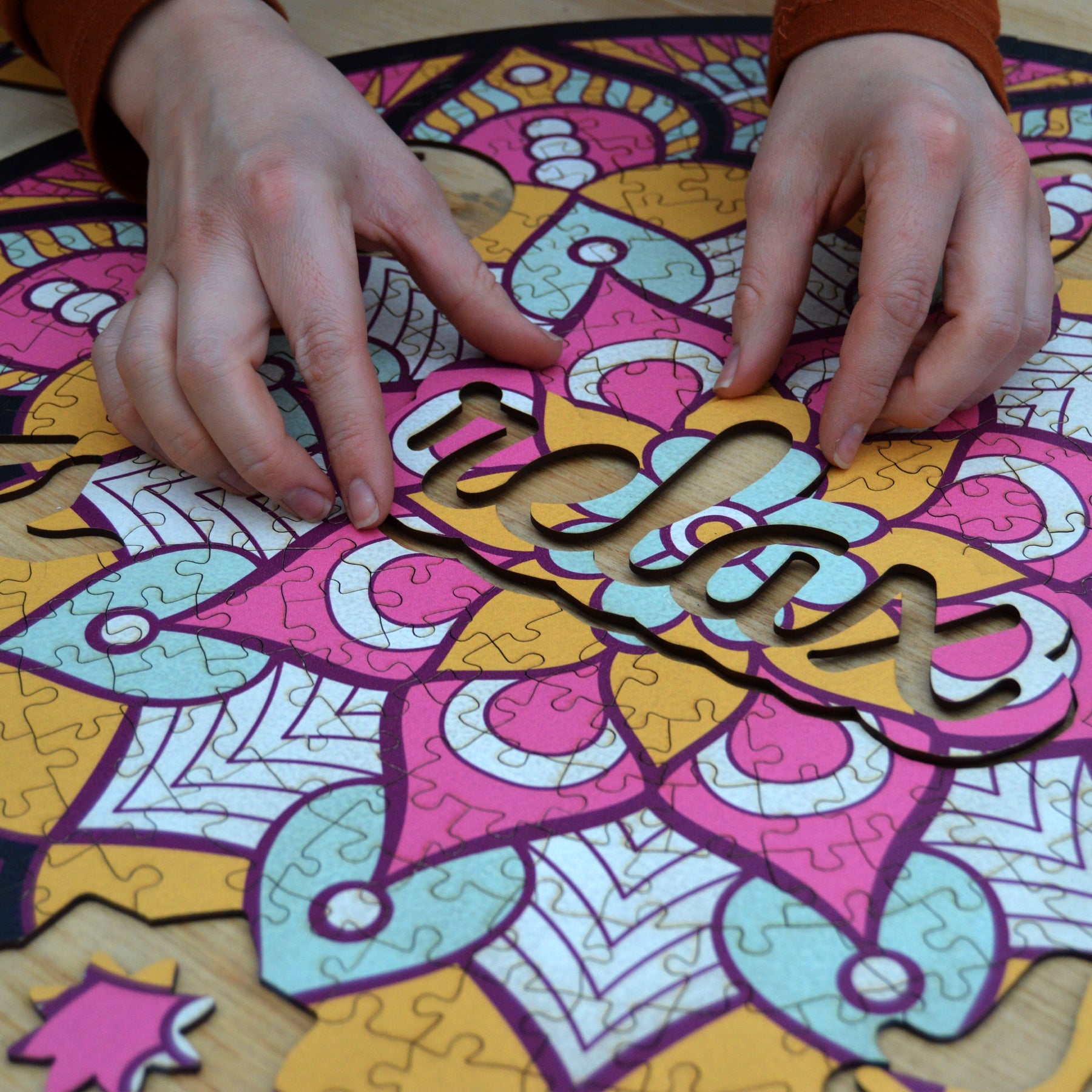 hands holding jigsaw pieces of a colorful mandala wooden jigsaw puzzle with a geometrical design.